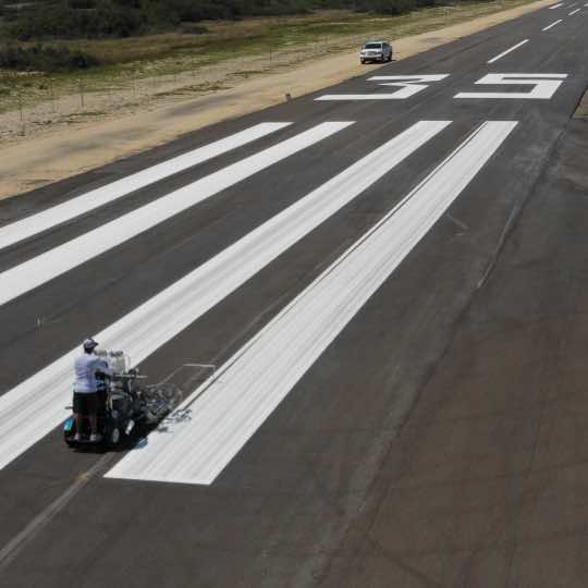 A worker applying markings to an airport runway.